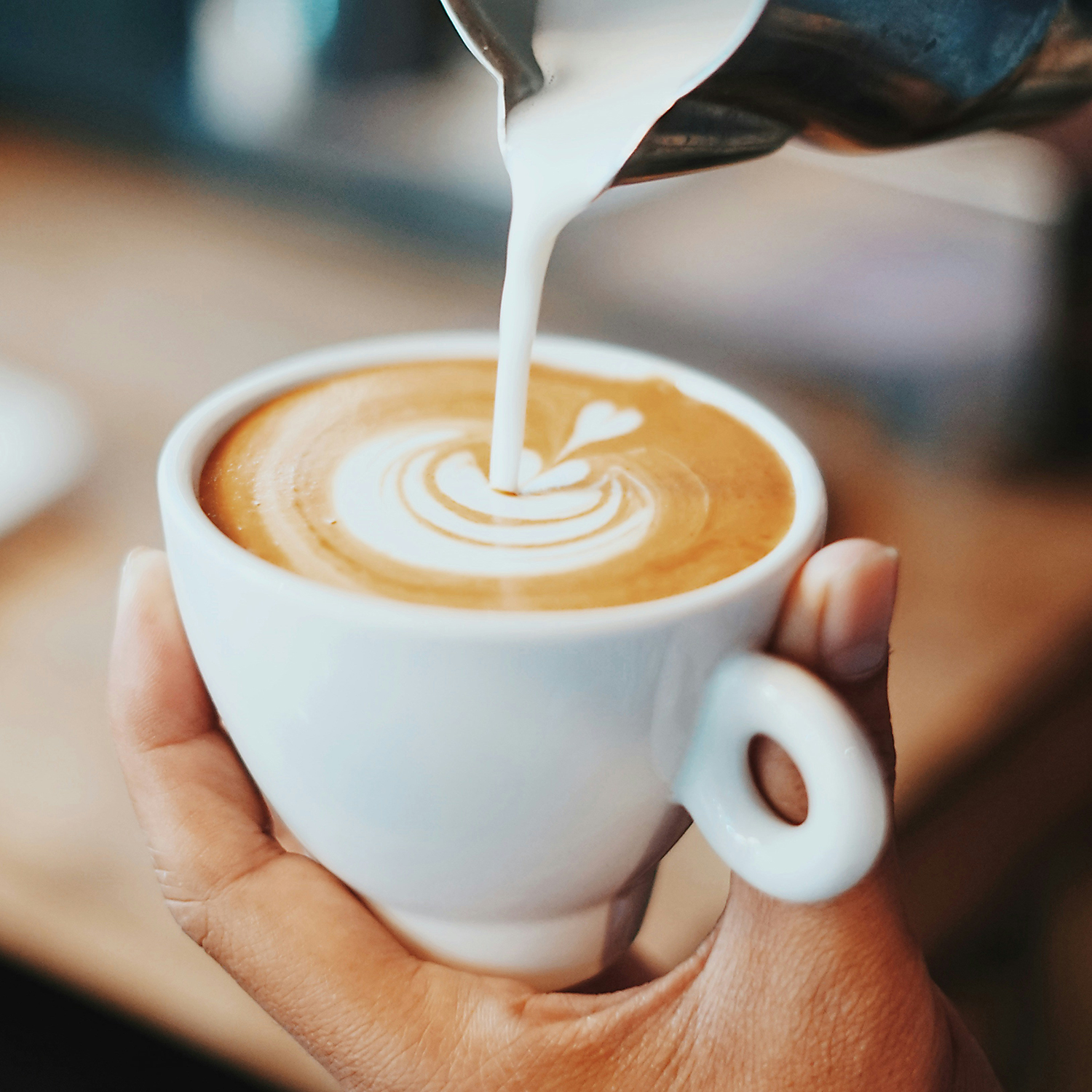 Gewerbeverein-Bad-Wimpfen-Cafe Nahaufnahme einer Kaffeetasse, in die aufgeschäumte Milch gegossen wird Gewerbeverein Bad Wimpfen